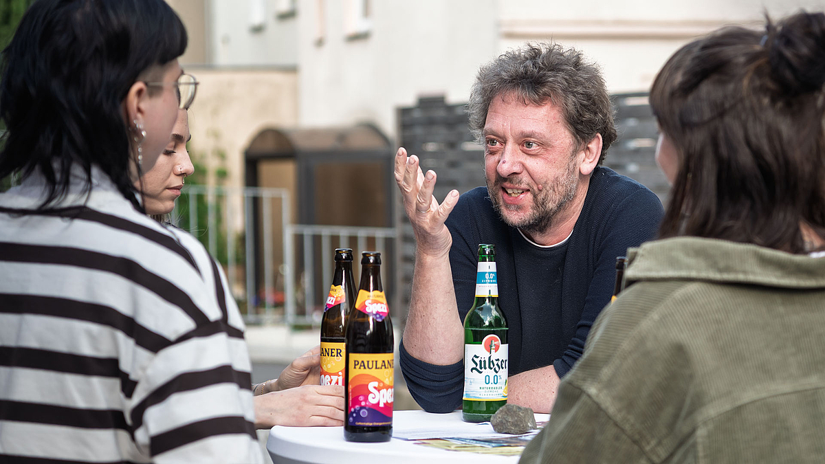 Im Gespräch: Professor Stephan Beetz, Dekan der Fakultät Soziale Arbeit mit „seinen“ Studentinnen. Eine männliche und drei weibliche Personen an einem Stehtisch, auf dem Getränkeflaschen stehen.