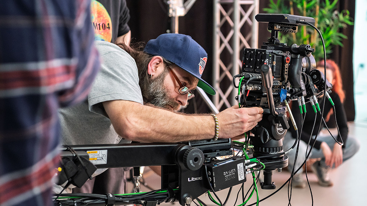 Eine männliche Person beugt sich über eine Kamera, die an einem Galgen montiert ist, und hantiert daran.