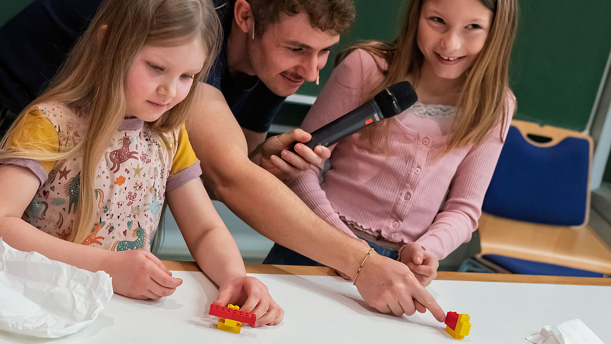 Blick auf zei der Kinder un dihre Lego-Enten. Zwischen den Kindern beugt sich der Moderator mit seinem Mikrofon herunter.