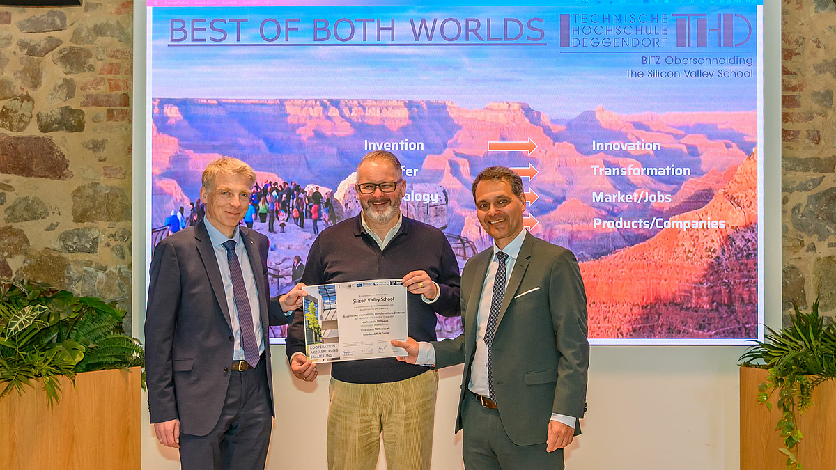 Drei männliche Personen halten eine Urkunde. Im Hintergrund ist ein Foto vom Grand Canyon zu sehen mit der Überschrift "Best of Both Worlds" und weitren Begriffen.