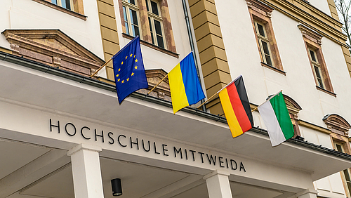 Am Hauptgebäude der Hochschule Mittweida sind über dem Eingang von links nach rechts die Flaggen der Europäischen Union, der Ukraine, Deutschlands und Sachsens gehisst.
