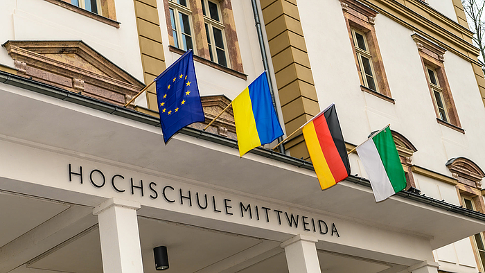 Am Hauptgebäude der Hochschule Mittweida sind über dem Eingang von links nach rechts die Flaggen der Europäischen Union, der Ukraine, Deutschlands und Sachsens gehisst.