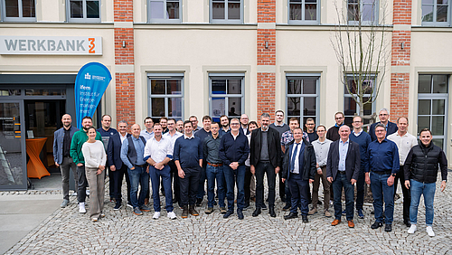 Gruppenfoto mit 32 Personen, darunter eine weibliche, vor einem Backsteingebäude mit der Aufschrift "Werkbank 32"  