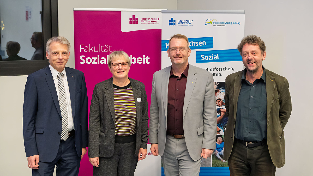 Gruppenbild mit drei männlichen und einer weiblichen Person am unteren Endes des Hörsaals vor Rollups mit "Fakultät Soziale Arbeit" und "Mittelsachsen Sozial"."