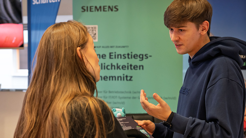 Junge weibliche und männliche Person im Gespräch vor Rollup "Siemens"