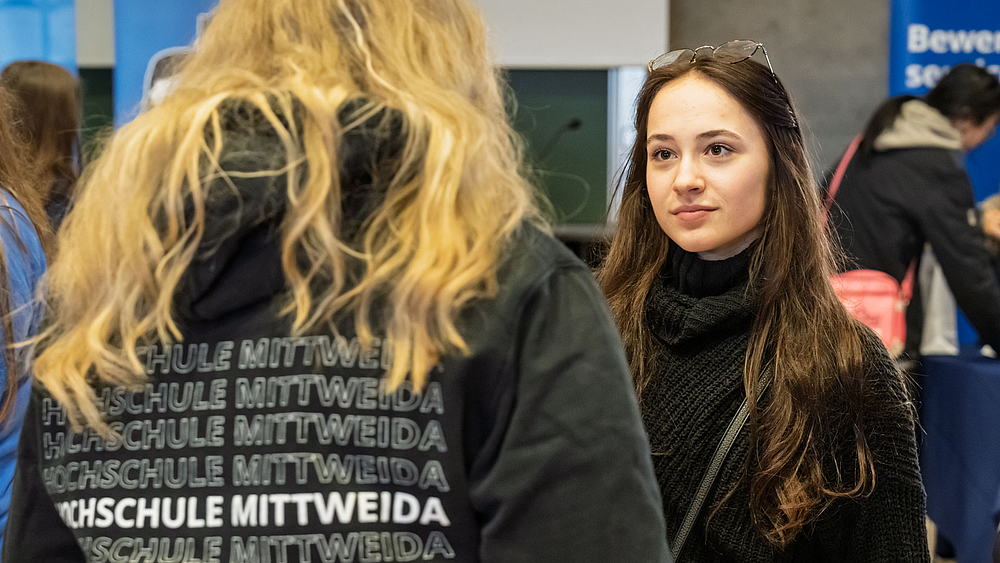 Zwei weibliche Personen im Gepräch. Auf dem Hoodie der einen ist mehrfach der Schriftzug "Hochschule Mittweida" zu lesen".