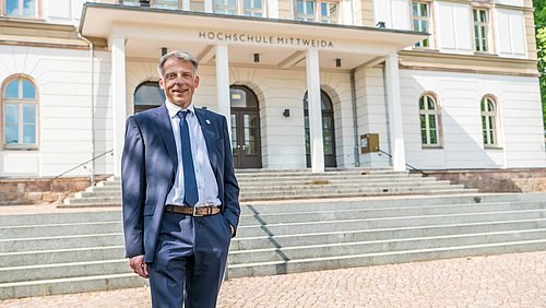 Gewählt: Prof. Dr. Volker Tolkmitt wird im Herbst das Amt des Rektors der Hochschule Mittweida übernehmen. Professor Tolkmitt steht freundlich lächelnd vor dem Hauptgebäude der Hochschule Mittweida. Er trägt einen blauen Anzug, ein weißes Hemd und eine blaue Krawatte.