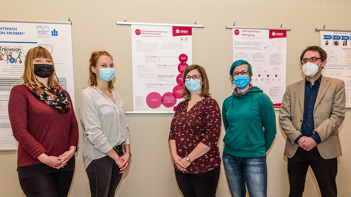 Das Foto zeigt die vier Studentinnen Lucie, Katharina, Laura und Doreen mit Professor Sebastian Noll vor einer Wand mit Forschungspostern..