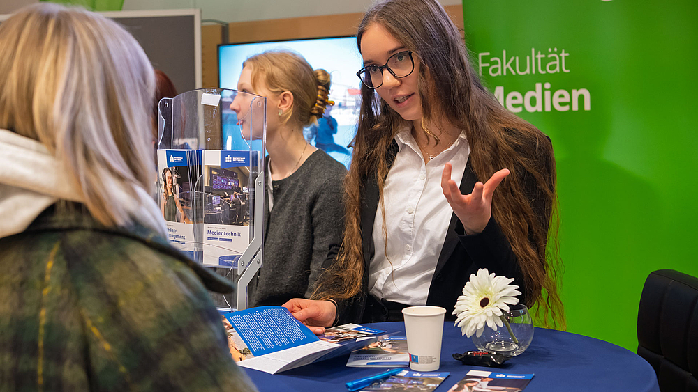 Junge Frau im Gespräch mit Besucherin vor Rollup "Fakultät Medien".