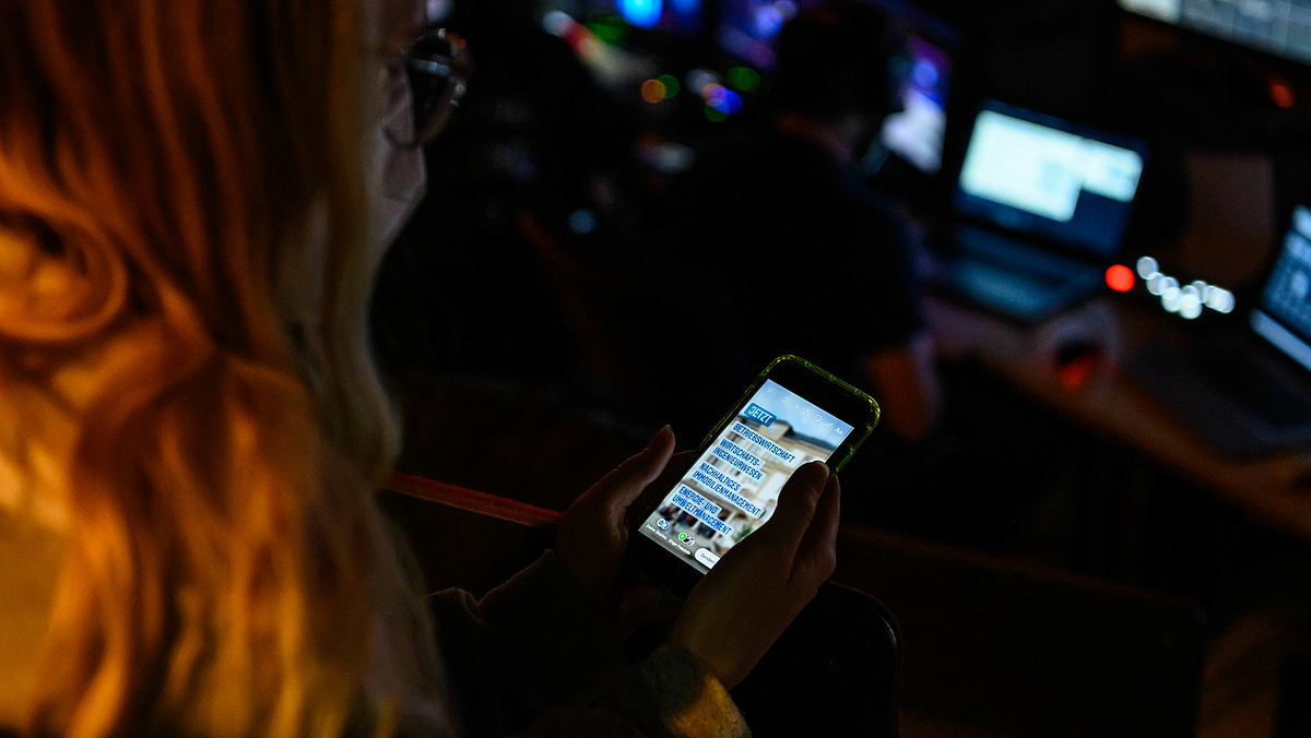 Auf dem Foto ist ein Smartphone in der Hand einer weiblichen Person zu sehen. Das Foto blickt über die Schulter un am angeschnittenen Kopf der Person auf das Display, auf dem im Instagramfesnter zu lesen ist: "JETZT BETRIEBSWIRTSCHAFT, WIRTSCHAFTSINGENIEURWESEN; NACHHALTIGES IMMOBILIENMANAGEMENT; ENERGIE- UND UMWELTMANAGEMENT".