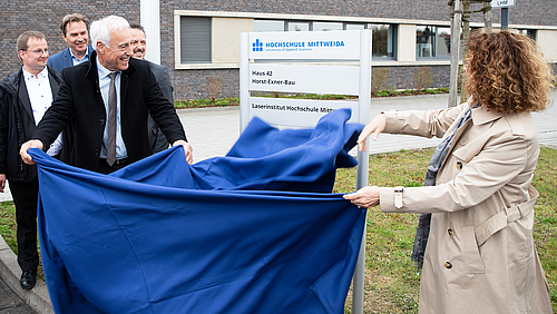 Professor Horst Exner enthüllt gemeinsam mit seiner Ehefrau das zuvor mit einem blauen Tuch verdeckt Schild mit der Aufschrift "Horst-Exner-Bau".