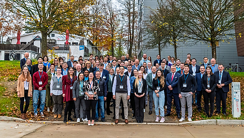 Gemeinsam gut aufgestellt: der neue Deutschlandstipendium-Jahrgang 2024/25 der Hochschule Mittweida mit geförderten Studierenden und ihren Förder:innen. Eine Menschengruppe mit rund 90 überwiegend lachenden Personen steht auf einem ansteigenden Weg und dem Rasen links und rechts davon. Im Hintergrund befinden sich Gebäude und weitgehend entlaubte Bäume.