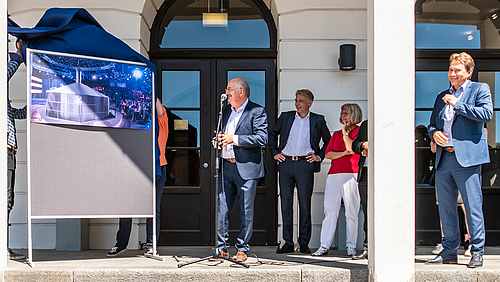 Skandal enthüllt. Lösung enthüllt: Rektor Ludwig Hilmer, Prorektor Volker Tolkmitt, Kanzlerin Sylvia Bäßler und Oberbürgermeister Ralf Schreiber und die neue Nutzung des Medienzentrums der Hochschule Mittweida. Das Foto zeigt die erfolgete Enthüllung einer Fotomontage, auf der ein Sudkessl im Fernsehstudio zu sehen ist. Die umstehenenden Personen freuen sich.