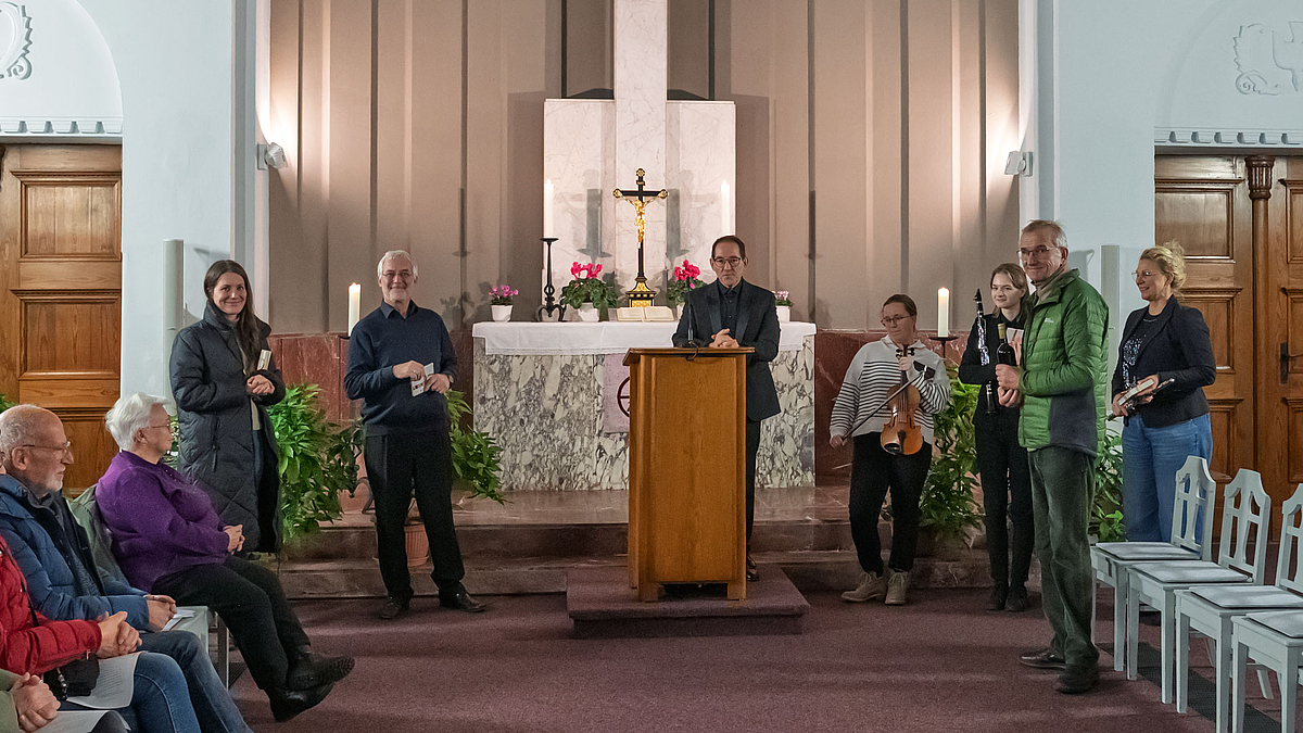 Alle Mitwirkenden und eine weitere männliche Perso den Zuhörenden zugewandt vor dem Altar.