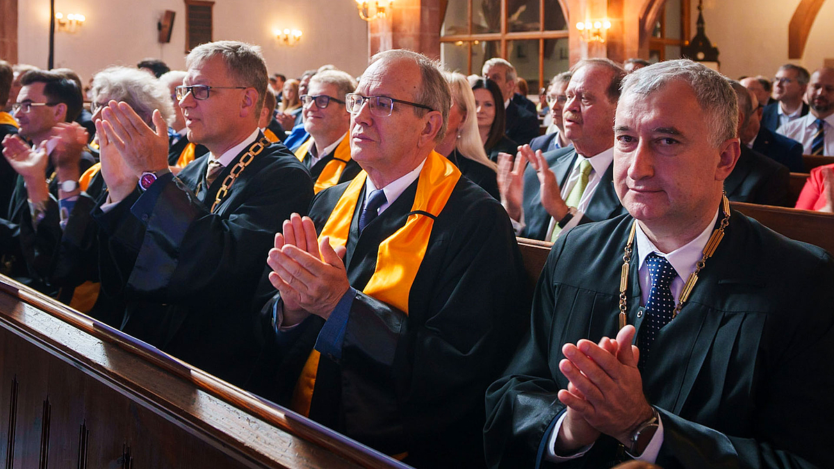 Professor Anatoly Ivanovich Kovalev (2.v.r.) reiste von Odessa nach Mittweida, um der Investitur von Professor Volker Tolkmitt beizuwohnen. Mehrere Professoren applaudieren. Sie tragen Talare und sitzen auf Kirchenbänken in der Stadtkirche Mittweida.