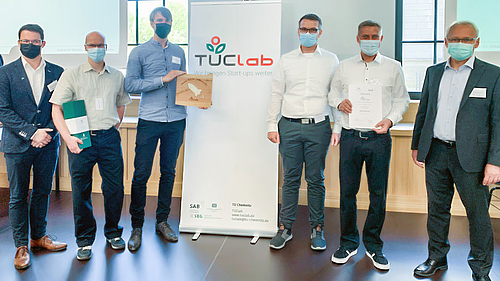TUClab-Award 2021 für das ANTACON-Team (Foto: TUClab) Das Fotos zeigt sechs männliche Personen mit Corona-Maske links und rechst von einem Rollup mit der Aufschrift "TUClab". Drei der Personen halten Urkunden und ein Geschenk.