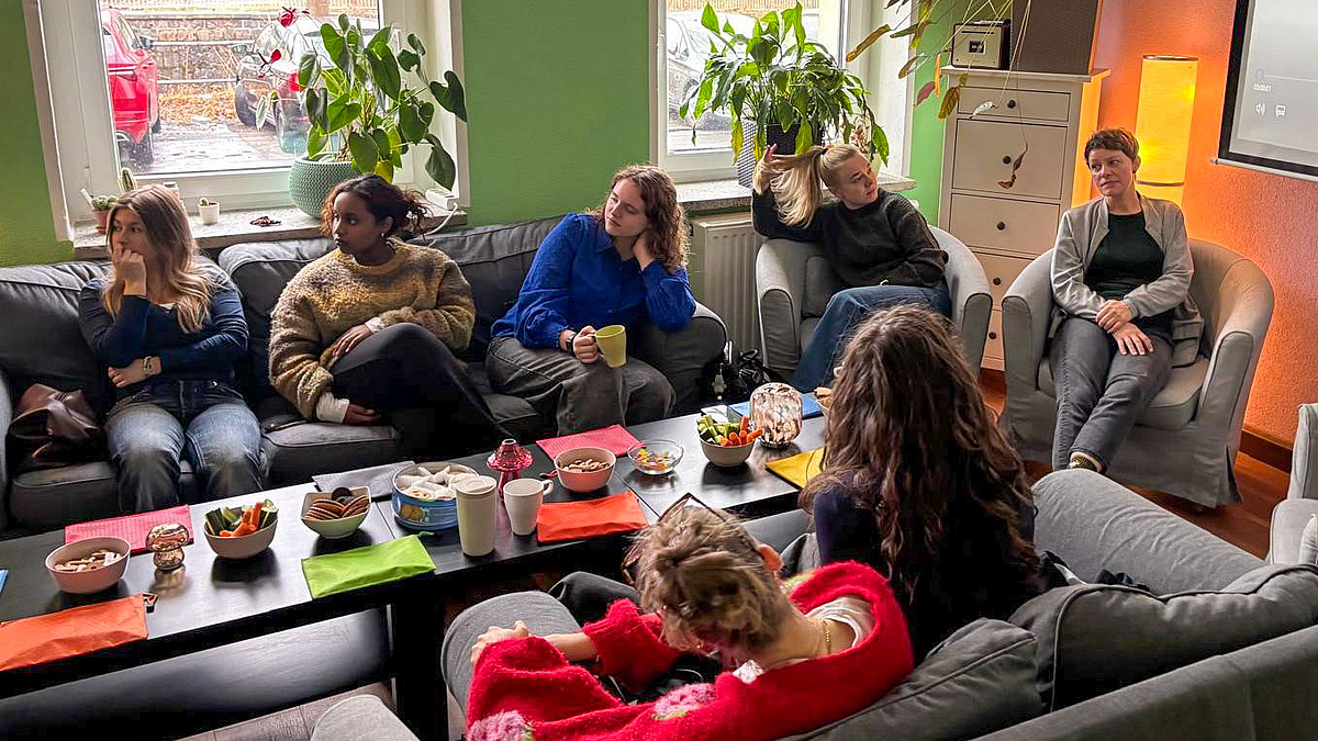 Sieben Personen auf Sofas und Sesseln  um einen Coucthtisch mit Gebäckschalen.