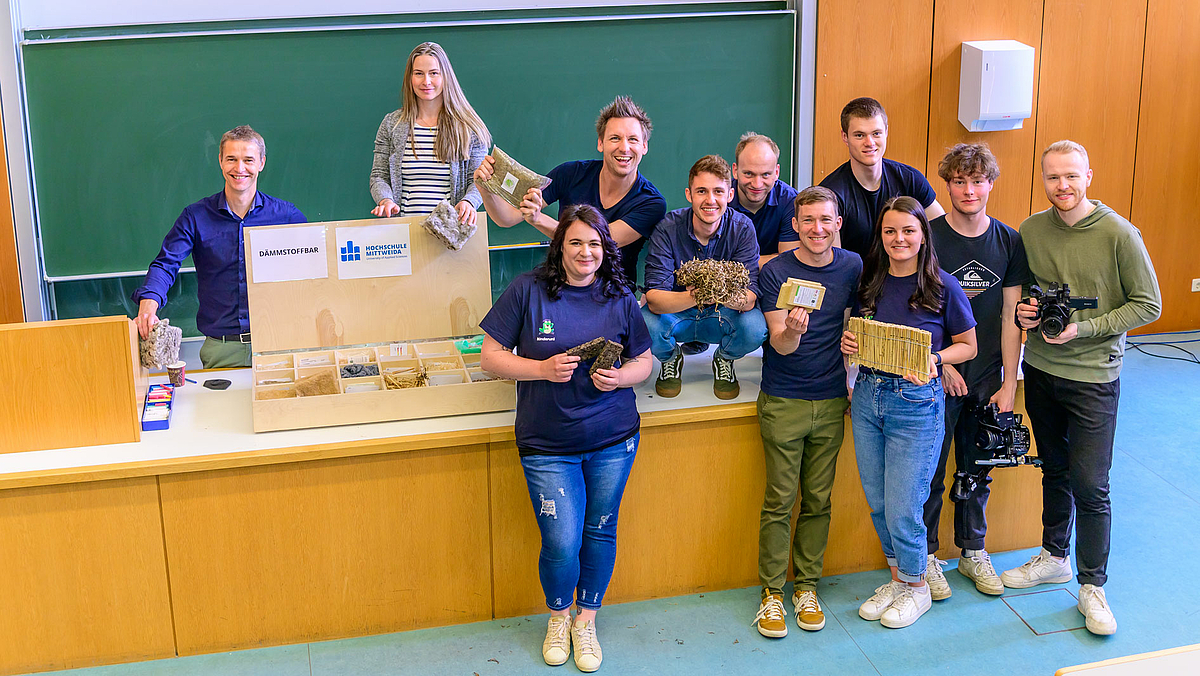 Das Gruppenfoto zeigt neben den Dozent:innen neun weitere junge Menschen vor und auf dem Hörsaalpult.