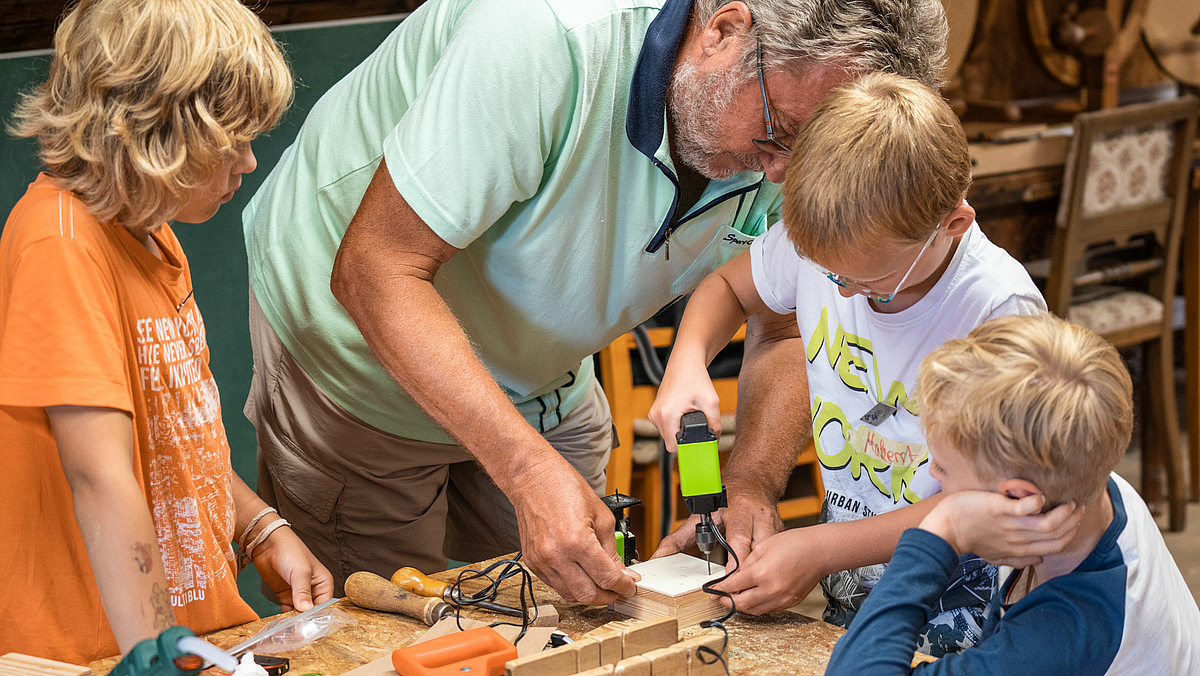 Das Foto zeigt drei Kinder und einen älteren Mann, den emeritierten Professor Hans-Gerhard Kretzschmar, der den Kindern beim Bohren für das Holzgehäuse einer Taschenlampe hilft.