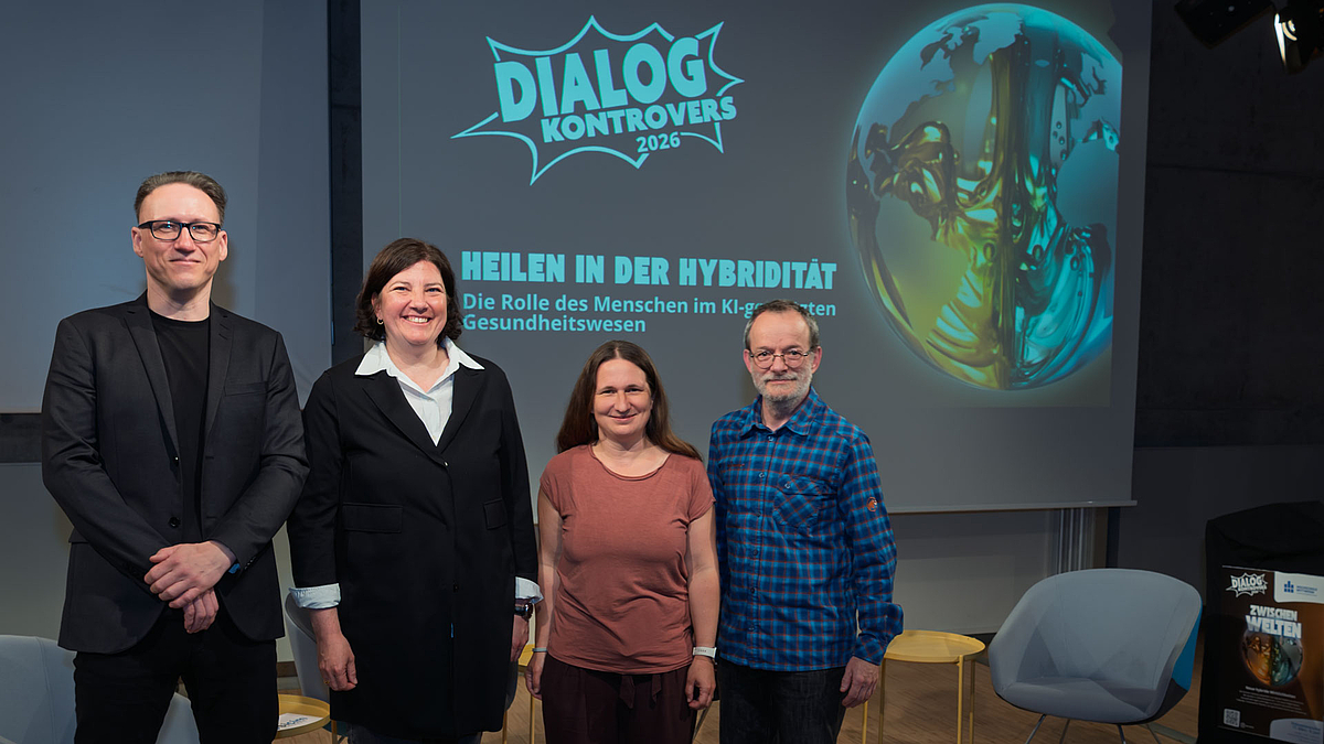 Dr. Maximilian Bretschneider, Professorin Christine Rummel-Kluge, Dr. Marika Kaden und Professor Thomas Villmann (v.l.n.r.) „bestritten“ klug und erkenntnisreich den „Dialog Kontrovers“ zum hochaktuellen Thema „KI in der Medizin“. Zwei weibliche und zwei männliche Personen stehen lächelnd vor der Leinwand hinter ihnen, die das Logo des Dialog Kontrovers und das aktuelle Thema „Heilen in der Hybridität. Die Rolle des Menschen im Kl-gestützten Gesundheitswesen“ zeigt.