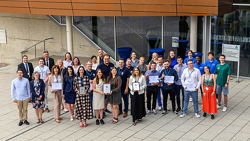 Finale des EURECA-PRO STEM Innovation Contests an der Hochschule Mittweida. Drei Siegerteams und ein gewinnender Gedanke: die europaweite Zusammenarbeit von Hochschulen für mehr Nachhaltigkeit. 34 junge Menschen stehen freudestrahlend vor einem Gebäude. Einige halten Urkunden und glänzende Preissymbole in den Händen.