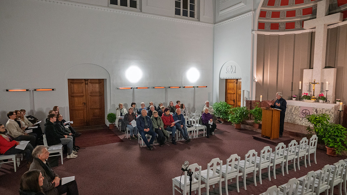 Blick in den Kapellentaum auf Zuhörende und eine männliche Person am Rednerpult.