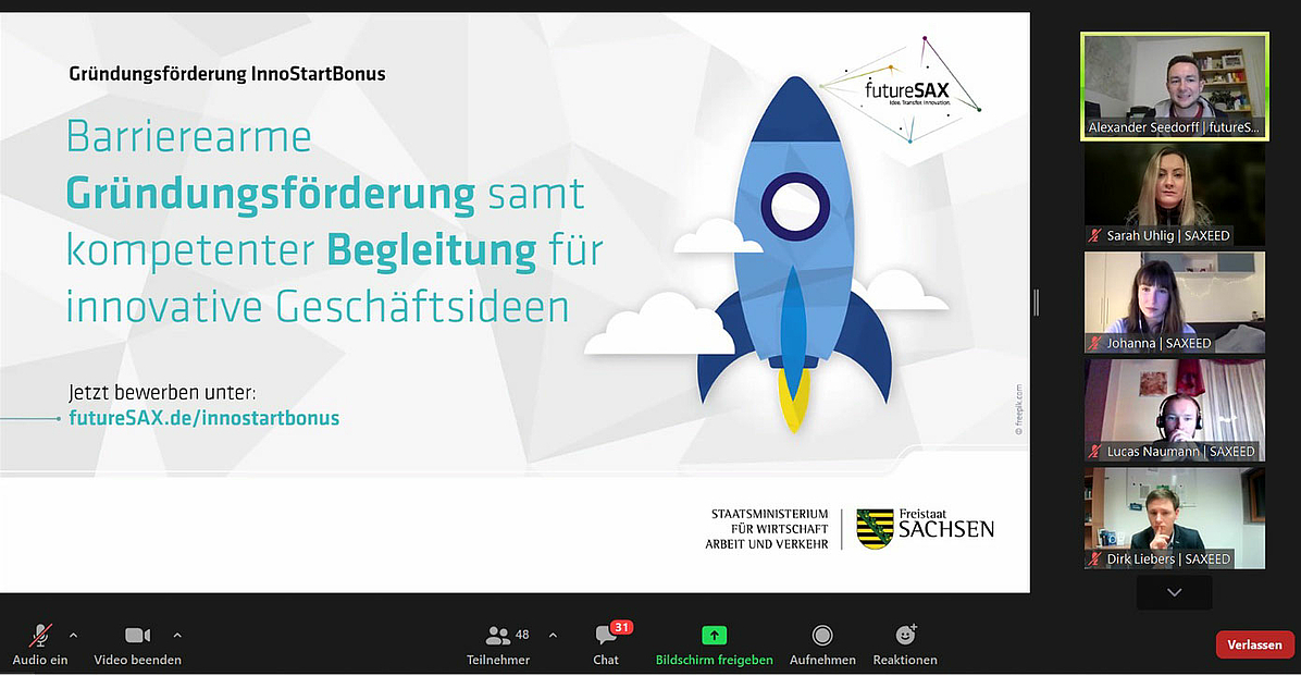 Auf dem Zoom-Screenshot ist links eine Powerpointfolie zu sehen mit dem Text: „Gründungsförderung InnoStartBonus. Barrierearme Gründungsförderung samt kompetenter Begleitung für innovative Geschäftsideen. Jetzt bewerben unter futureSAX.de/innostartbonus“. Der Text ist illustriert mit einer aufsteigenden bunten Rakete. Rechts sind untereinander fünf Kamerabilder von Teilnehmenden angeordnet, zuoberst der Referent