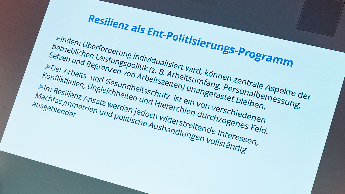 Foto einer projizierten Folie mit der Überschrift „Resilienz als Ent-Politisierungs-Programm.“