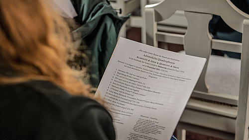 Blick über die Schulter einer sitzenden Person, die ein Blatt mit der Programmabfolge in der Hand hält. 