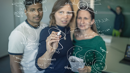 Zwei Frauen und ein Mann stehen vor einer Glasscheibe, auf die sie mathematische Formeln schreiben. Im Hintergrund steht ein Professor an einer klassischen Tafel.