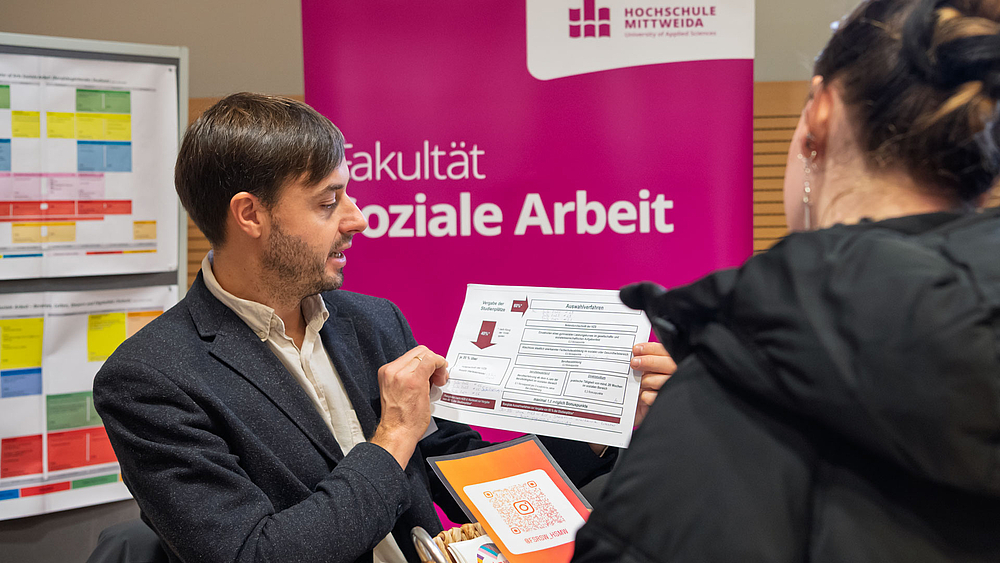 Männliche Person vor Rollup "Soziale Arbeit" zeigt ein Papier zum Thema "Auswahlverfahren".
