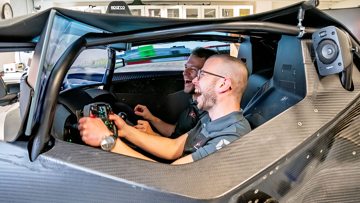 Zwei junge Männer, ausgelassen lachend, im Cockpit der Simulationsplattform.