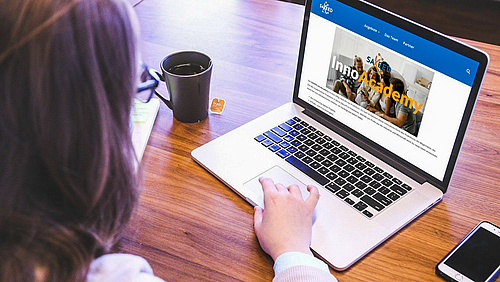 InnoAcademy – das Praktikum für die eigenen Ideen bei Unternehmen in der Region. Jetzt noch bis 31.12. bewerben! Das Foto zeigt eine Person im Anschnitt von hinten. Vor ihr auf dem Tisch sind von links eine Tasse mit Tee, ein Laptop und ein Smartphone zu sehen. Die Finger der rechten Hand berühren das Touchpad des Laptops, auf dessen Bildschirm die Startseite der Saxeed-InnoAcademy geöffnet ist.