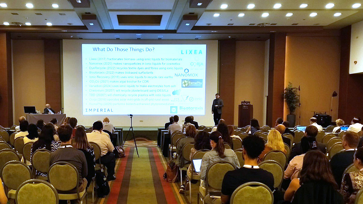 An der International Conference on Responsible Consumption and Production beteiligen sich auch Forschende, die nicht aus einer der EURECA-PRO-Hochschulen stammen. Ein Mann spricht vor einer großen Leinwand auf einem Podium. Die Leinwand zeigt viel Schrift auf weißem Grund. Im Vordergrund sitzen Menschen in circa zehn Sitzreihen im Auditorium.