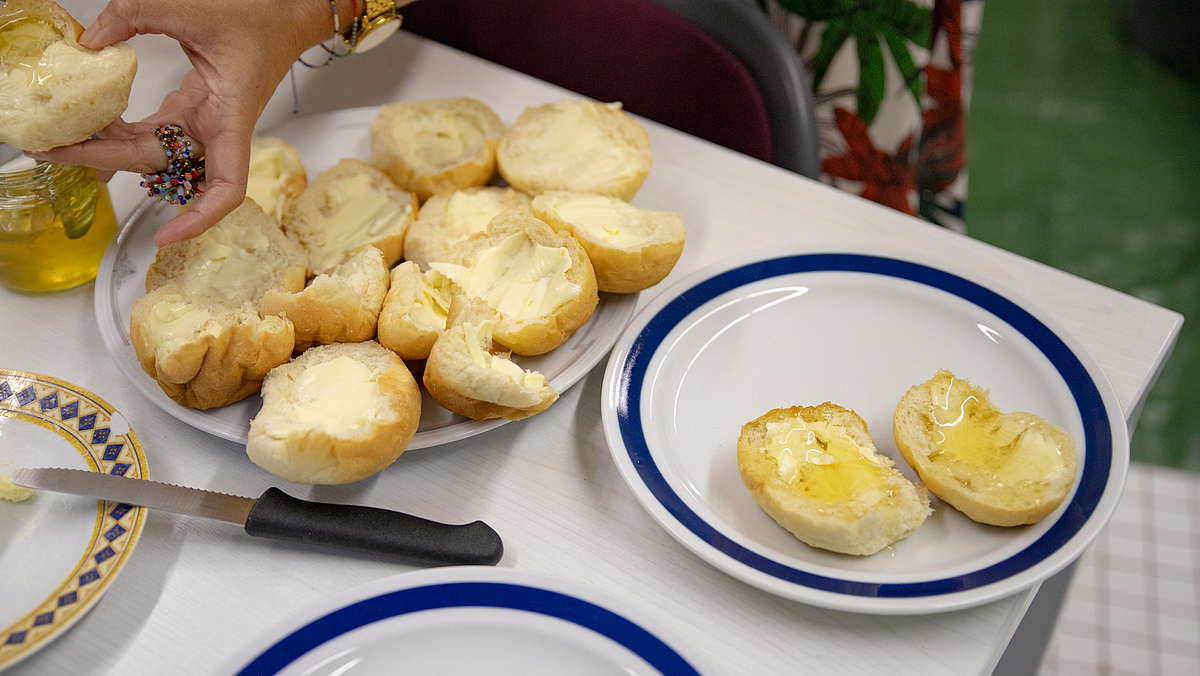 Auf einem Teller befinden sich zehn halbe Brötchen mit Butter, auf dem danebenstehenden zwei mit Butter und Honig.