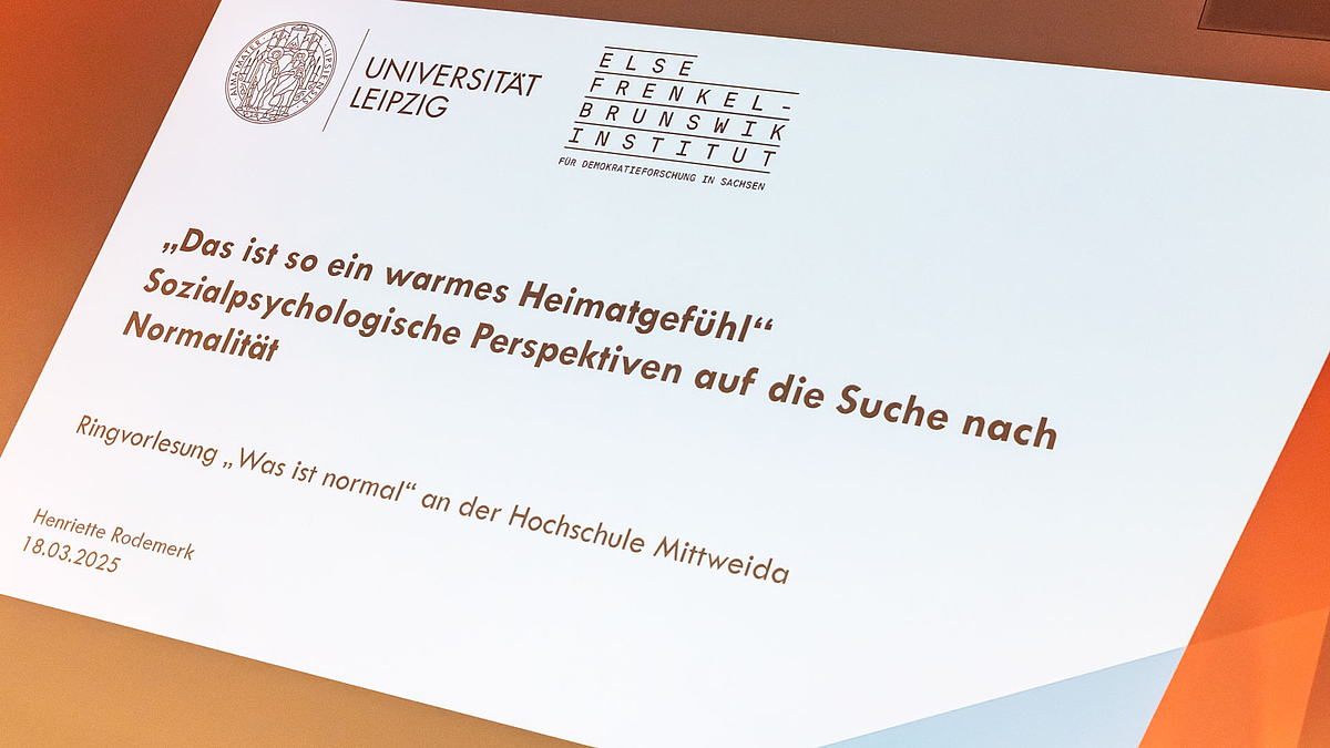 Foto einer projizierten Folie mit der Überschrift zur Vorlesung: „Das ist so ein warmes Heimatgefühl“ – Sozialpsychologische Perspektiven auf die Suche nach Normalität.