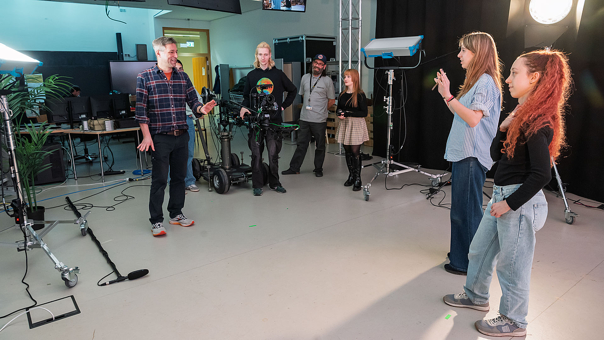 Studioraum mit Dozent und und fünf weiteren Personen, die mit ihm agieren.