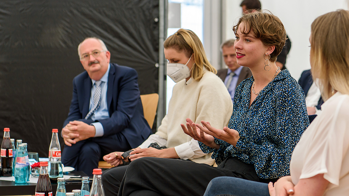 Eine Studentin spricht. Neben ihr sitzt eine Kommilitonin mit Maske, dahinter hört Rektor Ludwig Hilmer den Ausführungen zu.