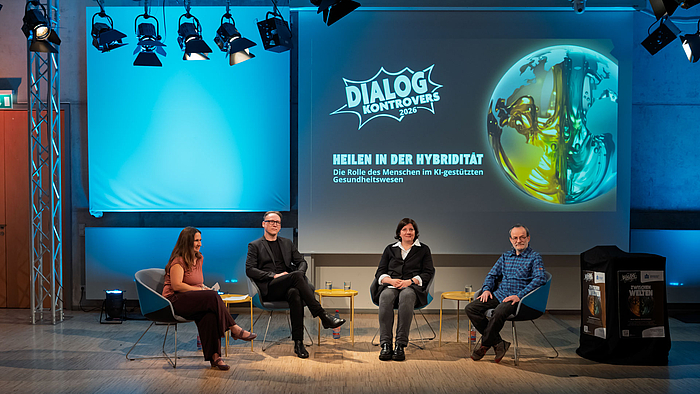 KI in der Medizin: Expert:innen aus der KI-Forschung, der Medizin und der Psychologie beim Dialog Kontrovers an der Hochschule Mittweida. Zwei weibliche und zwei männliche Personen in Sesseln in einem studioähnlichen Raum. Auf der Leinwand hinter ihnen ist das Logo des Dialog Kontrovers zu sehen und das aktuelle Thema „Heilen in der Hybridität. Die Rolle des Menschen im Kl-gestützten Gesundheitswesen“ zu lesen.