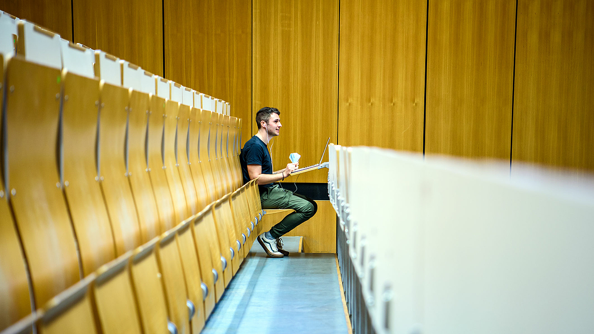 Das Foto zeigt Robin Dörrenbächer alleine am Ende einer langen Bankreihe eines ansonsten menschenleeren Hörsaals.