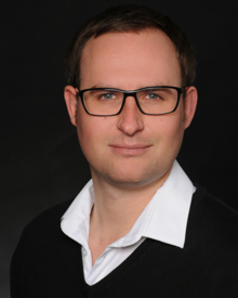 Prof. Dr. Janis Brinkmann betreut die Studierenden von medienMITTWEIDA als wissenschaftlicher Leiter. Janis Brinkmann schaut auf einem Porträtfoto vor schwarzem Hintergrund in die Kamera.