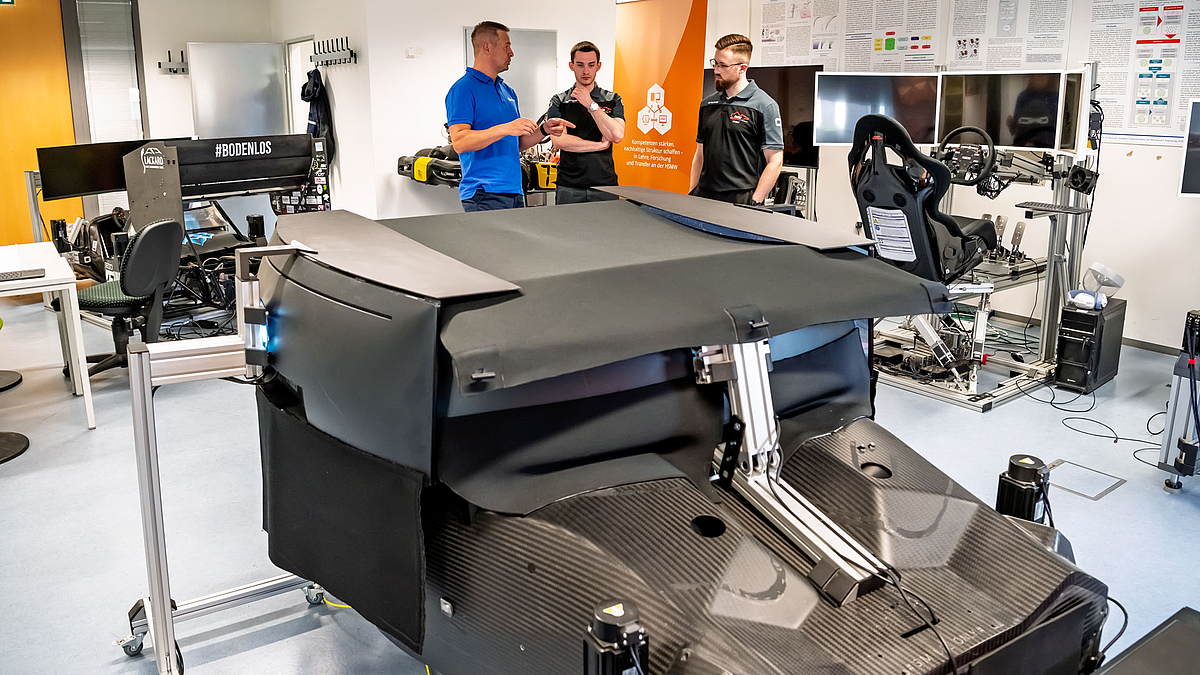 Blick von vorn auf die schwarz verkleidete Simulationsplattform. Im Hintergrund sind weitere Simulatoren mit Monitoren zu sehen.