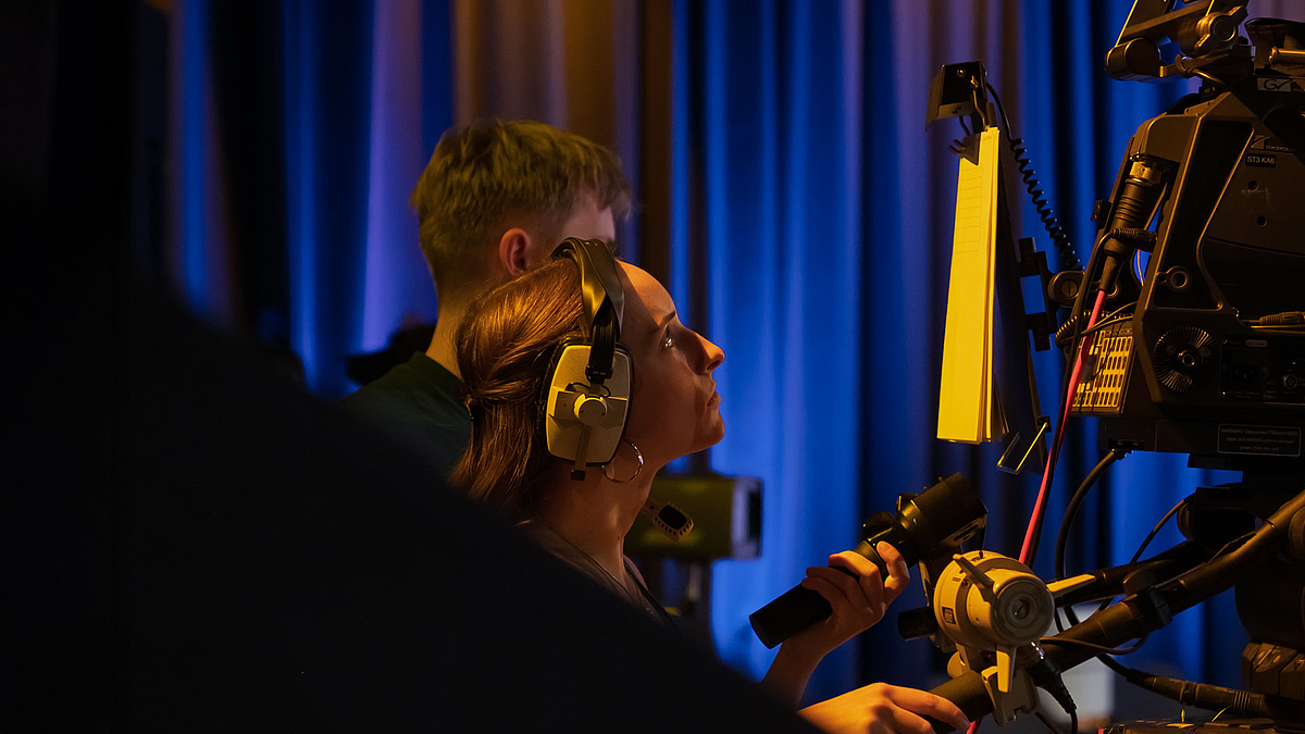 Seitlicher Blick auf eine junge weibliche Person, die konzentriert eine Studiokamera bedient.