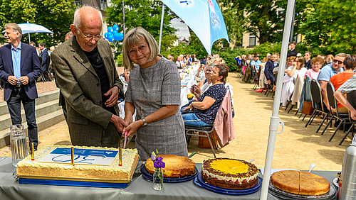 Ehrensache: Gründungsrektor Professor Reinhard Schmidt (84) schnitt zusammen mit Kanzlerin Sylvia Bäßler die Geburtstagstorte an. Das Foto zeigt eine männliche und eine weibliche Person. Sie fassen gemeinsam ein Messer an und schneiden eine Torte vor sich auf einem Tisch an, auf der eine große 30 zu erkennen ist. Im Hintergrund sind zahlreiche Menschen an langen Tafeln sitzend zu sehen.