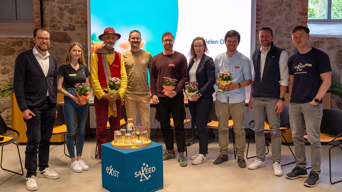 Gründungsgrün fürs Podium von Prof. Buser (l.) und Prof. Knauer und Dr. Liebers (2.u.1.v.r.) für Victoria Teuchert, Robby Hammer, Christian Atz, Lorenz Weil, Katrin Naumann, Richard Friedrich (v.l.n.r.). (Foto: Olivia Weinehl) Gruppenaufnahme mit neun Personen. Einige von ihnen haben einen Blumentopf in den Händen.