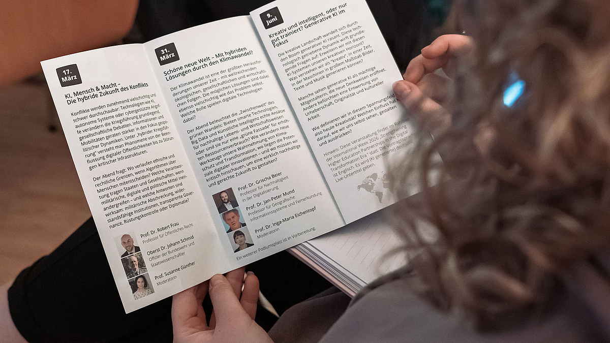 Blick über die Schulter einer weiblichen Person, die den aufgeschlagenen Dialog Kontrovers Flyer in den Händen hält. Zu sehen sind die Beschreibngen der ersten beiden und des letzten Abends.