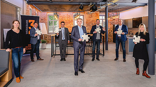 Die InitiatorInnen von NEXXT Mittweida gestalten die verschiedenen Puzzle-Teile der Unternehmensnachfolge. Sieben Personen stehen mit viel Abstand in einem loftartigen Raum. Sechs von ihnen halten je ein Puzzle-Teil in der Hand.