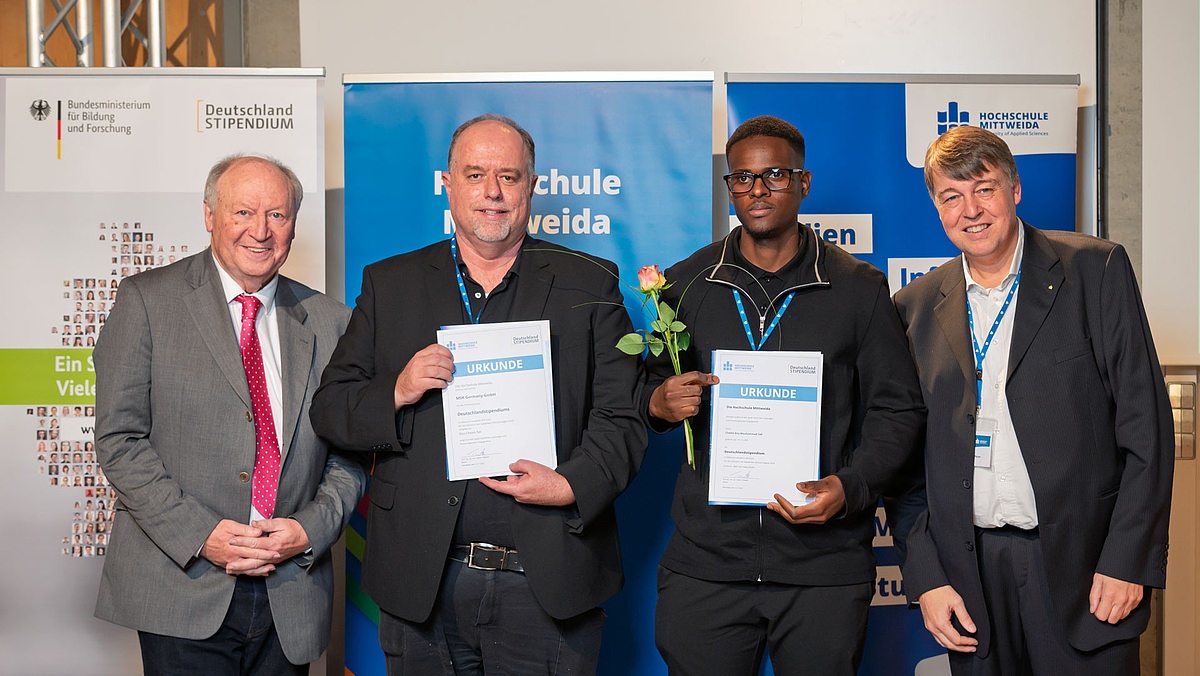 Vier männliche Personen, davon in der Mitte zwei mit Urkunden zwischen vor Rollups des Deutschlandstipendiums und der Hochschule Mittweida.