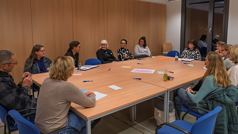 12 Personen an eionem großen Tisch im Gespräch