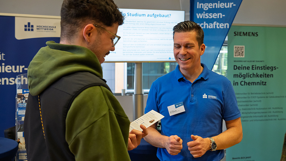 Männliche Personen im Gespräch vor Rollup "Ingenieurwissenschaften".